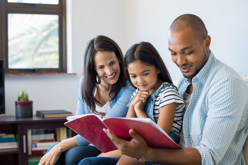 Young mom and dad read a book with their daughter.