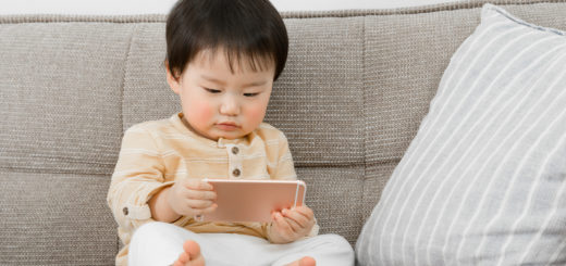 Young toddler holding and viewing a smart phone while sitting on the couch